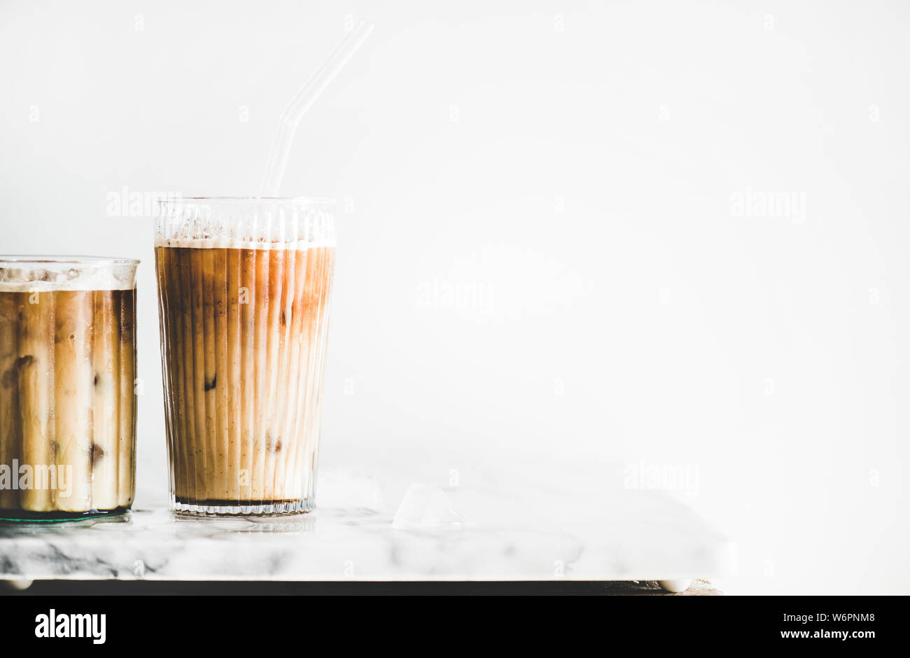 Homemade iced latte coffee in glasses with straws on marble table, white wall at background, copy space, close-up. Summer cold refreshing drink concep Stock Photo