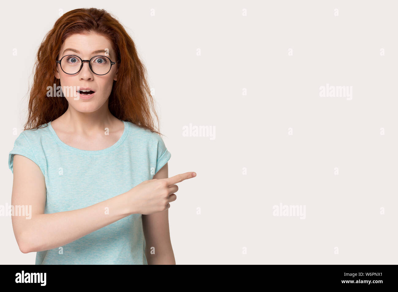 Red-headed female feels astonished point finger aside on copyspace Stock Photo