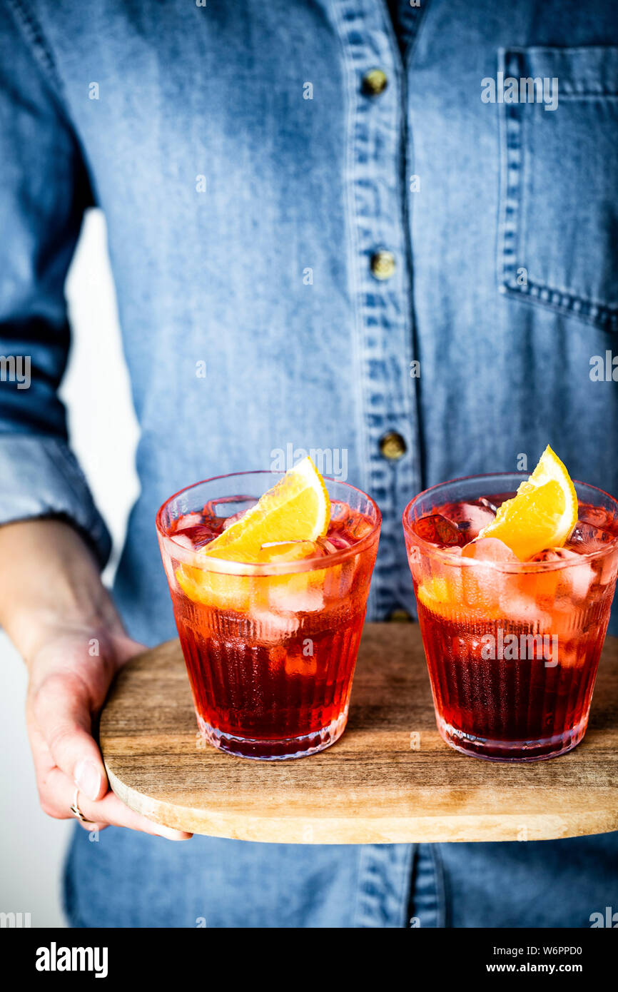 Negroni cocktail on a wooden tray, held by a person in a denim shirt Stock Photo