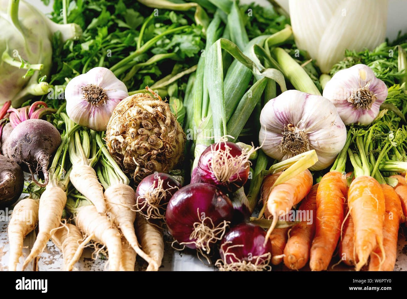 Variety of root garden vegetables carrot, garlic, purple onion, beetroot, parsnip and celery with tops over white marble background. Stock Photo