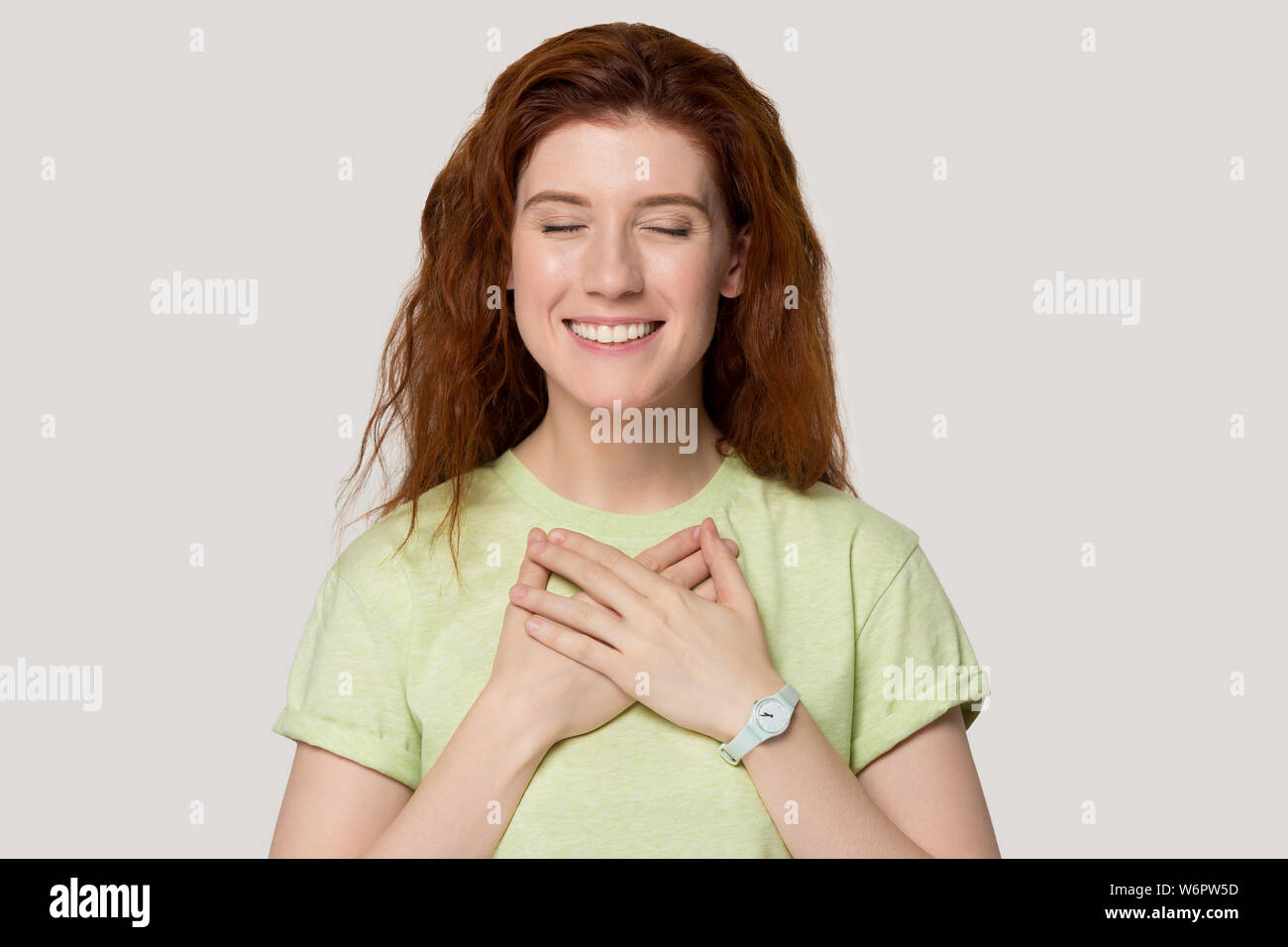 Female closing her eyes holds hands on chest feels gratitude Stock Photo