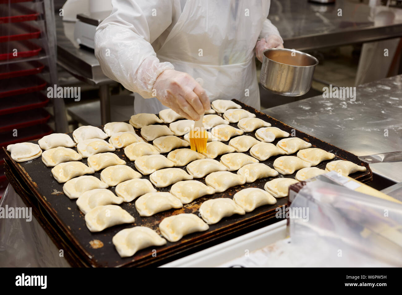 Pastry chef is cooking sweet buns, brushing with egg yolk Stock Photo