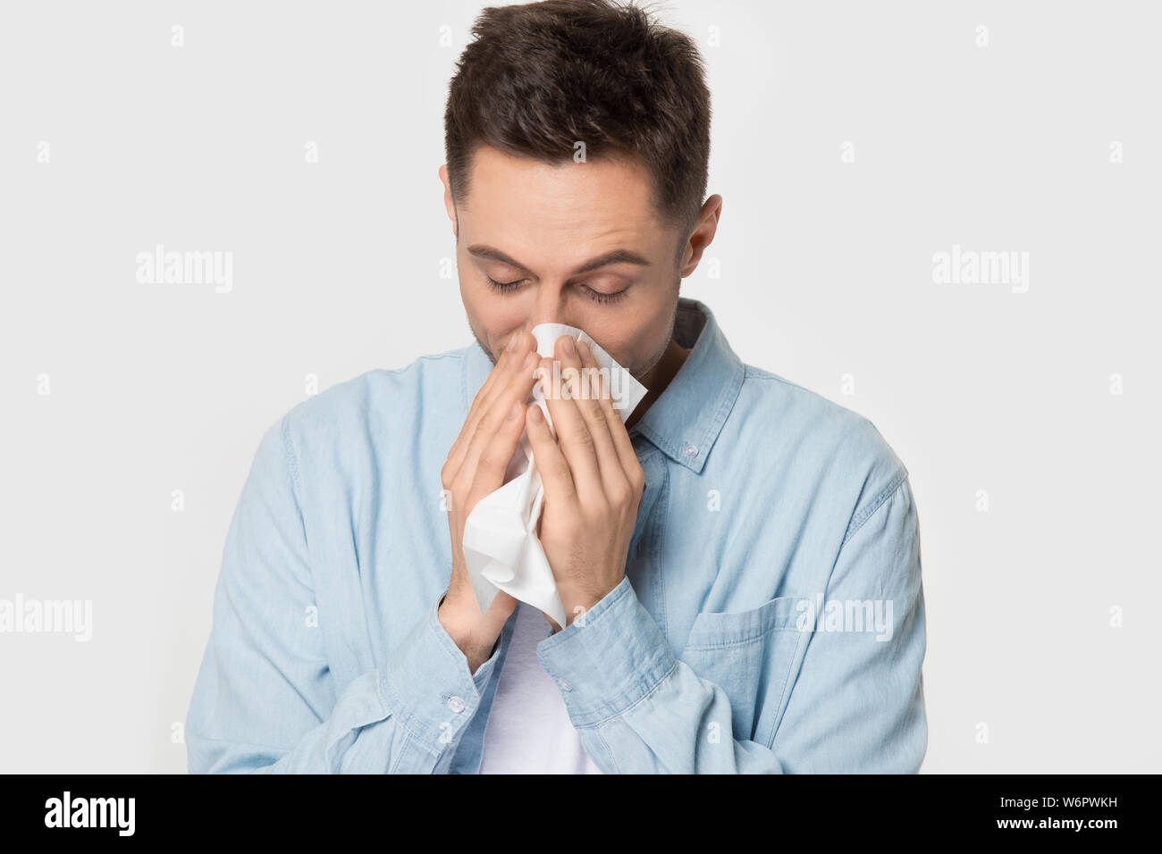 Sick guy holding handkerchief sneezing wiping nose studio shot Stock Photo