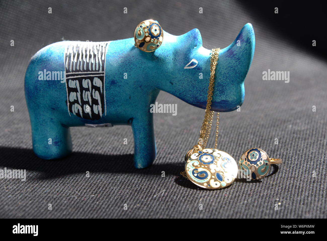jewellery on the  little blue rhino statue hold the jewellery holder blue necklace gold rings blue and gold rings with Gray background pretty animal Stock Photo