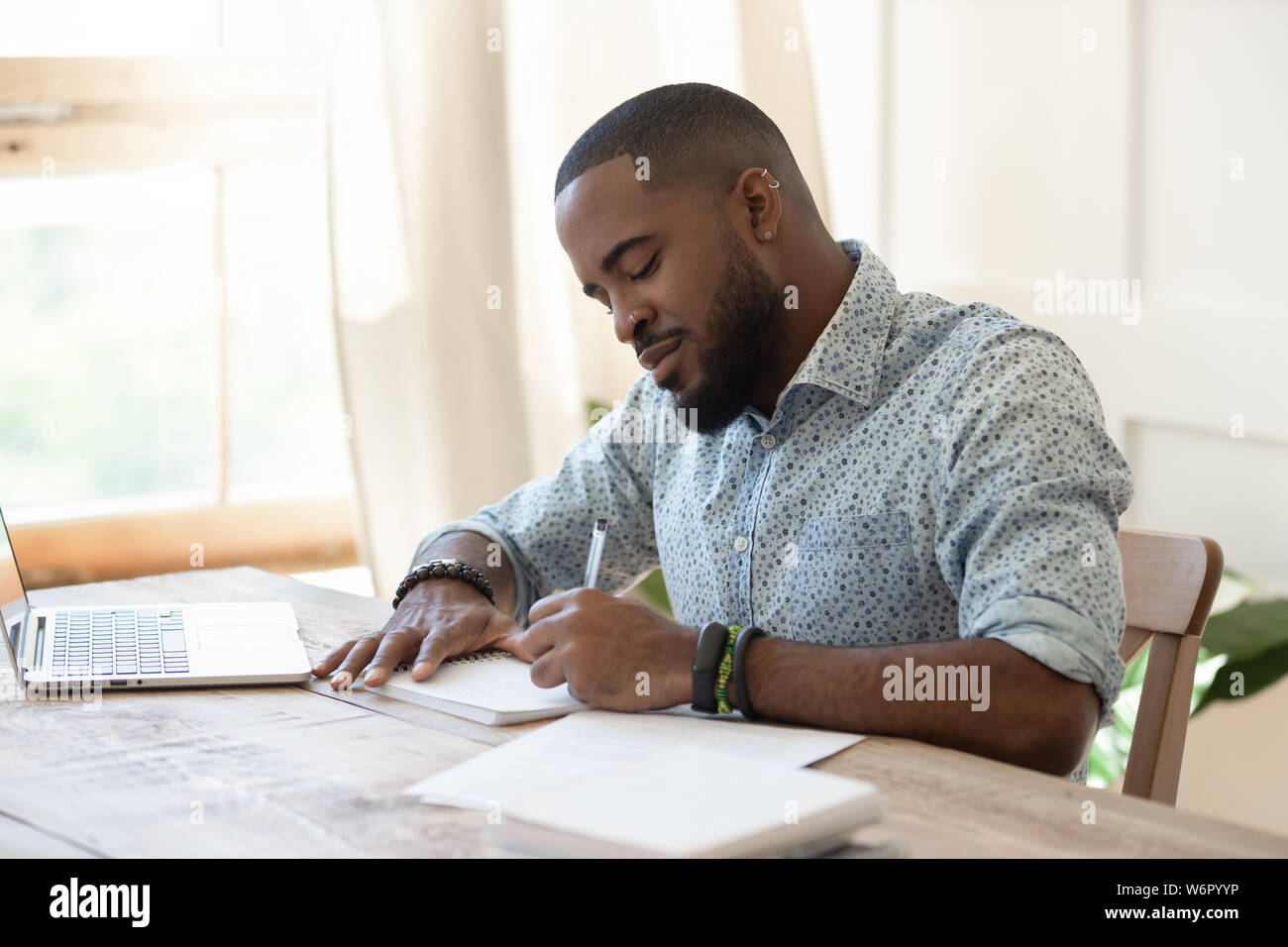 Focused african man student freelancer making notes studying with laptop Stock Photo
