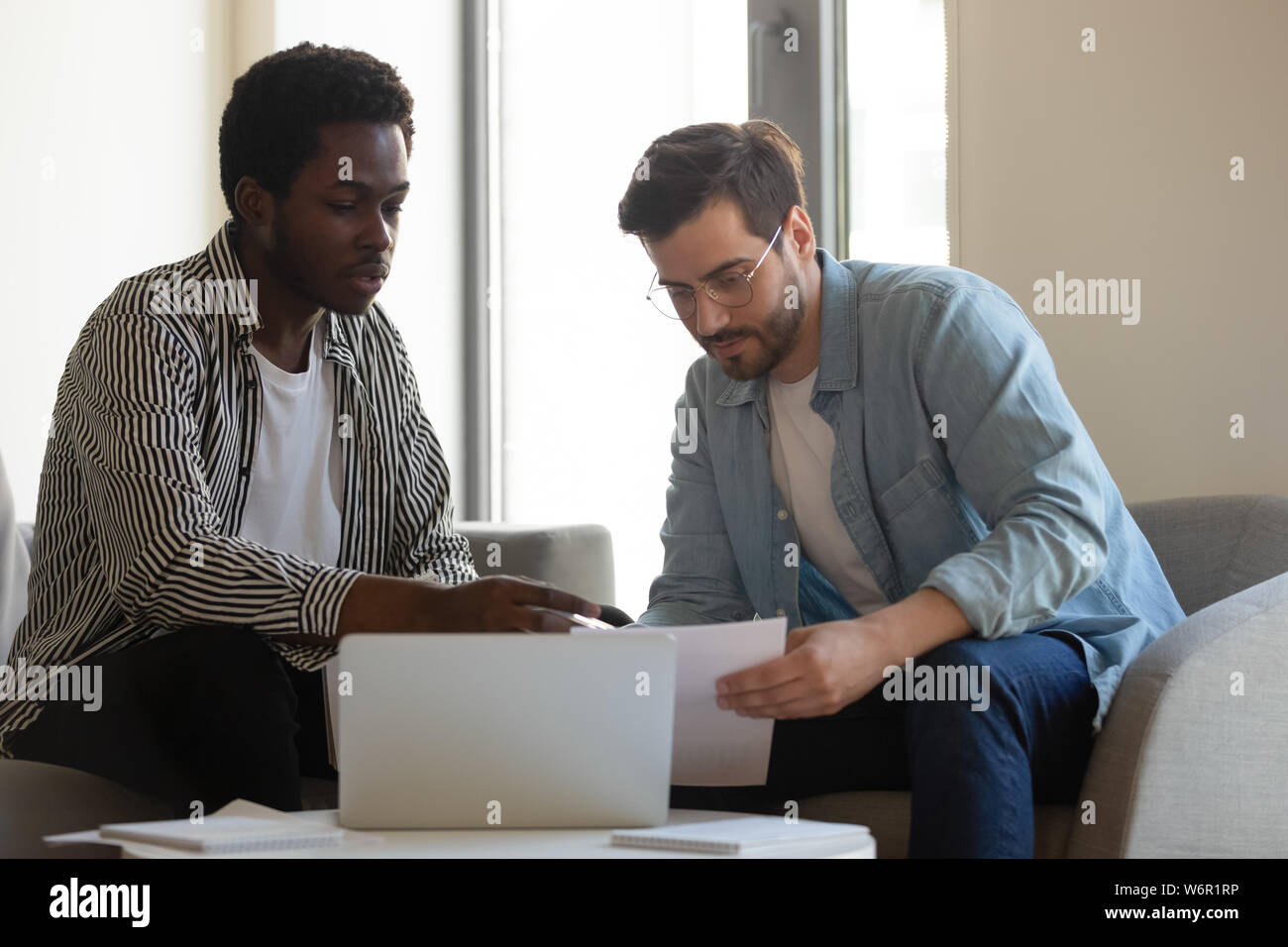 Focused african and caucasian male colleagues discussing paperwork report contract Stock Photo
