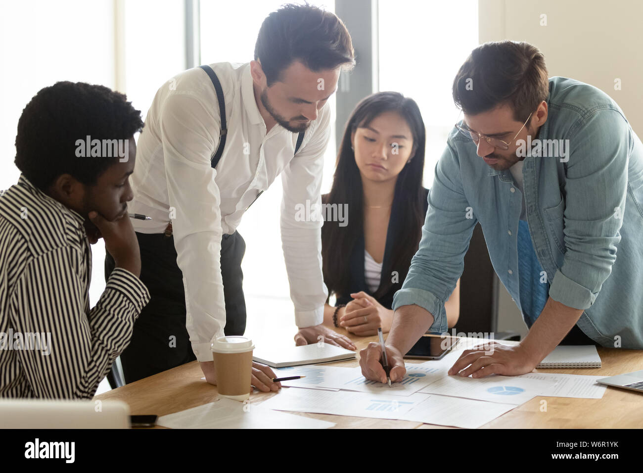 Focused multicultural team analyzing paperwork report gathered at office table Stock Photo