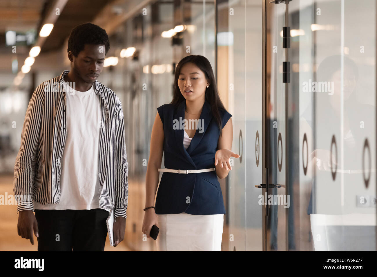 Two serious diverse colleagues talking walking in modern office hallway Stock Photo