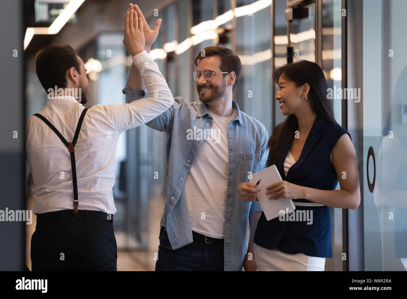 Friendly male colleagues giving high five talking in office hall Stock ...