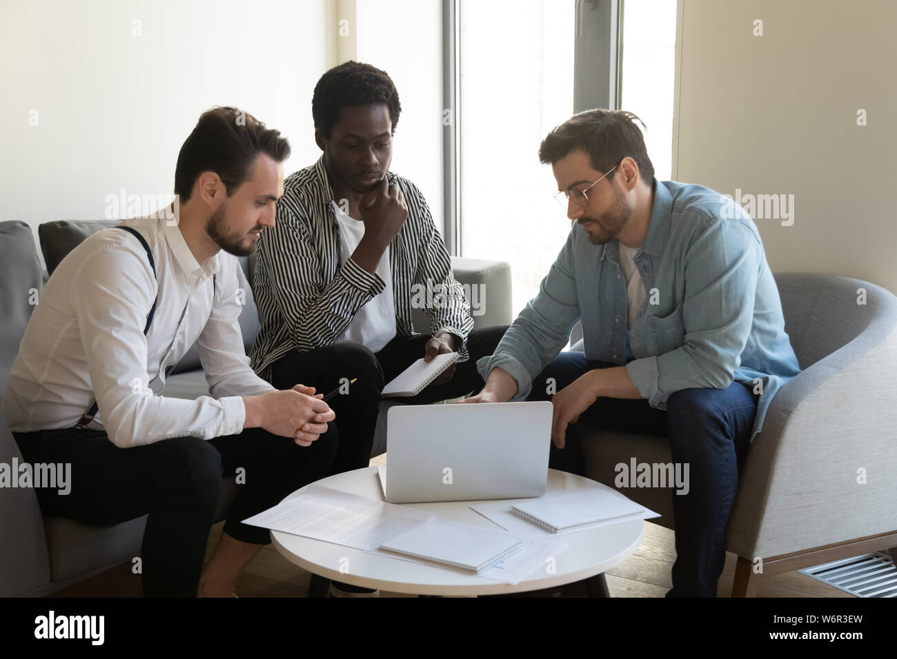 Three multiracial businessmen discuss online project look at laptop Stock Photo