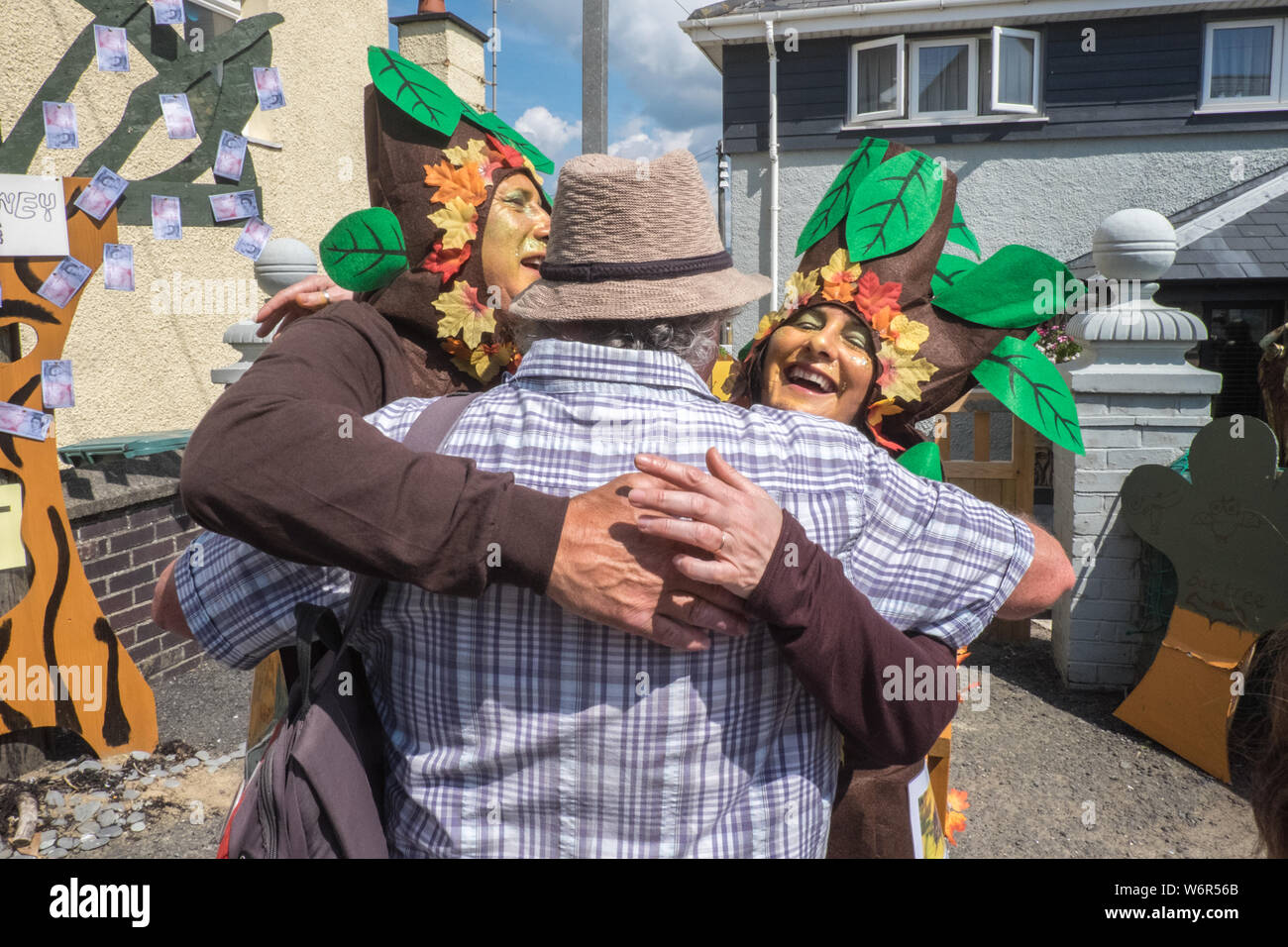 Guy in hat,gets a hug,from dressed up trees,tree huggers,hug a tree,with  Money Tree,in,background,on High Street,Borth,during,Famous,seaside,,resort,village,town,carnival,parade,at,Borth  Carnival,held,annually,annual,event,on,the,first,Friday,in,August ...