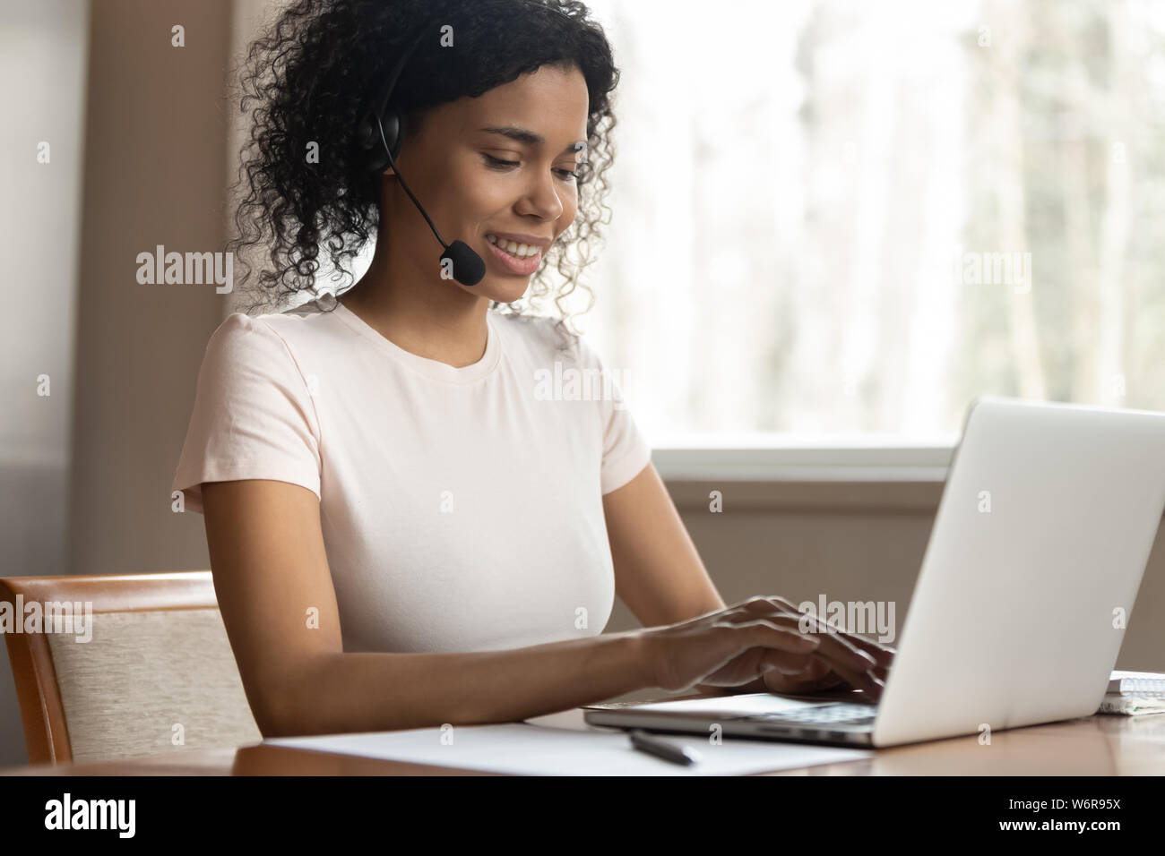 Young mixed race woman wearing headphones typing on computer Stock Photo