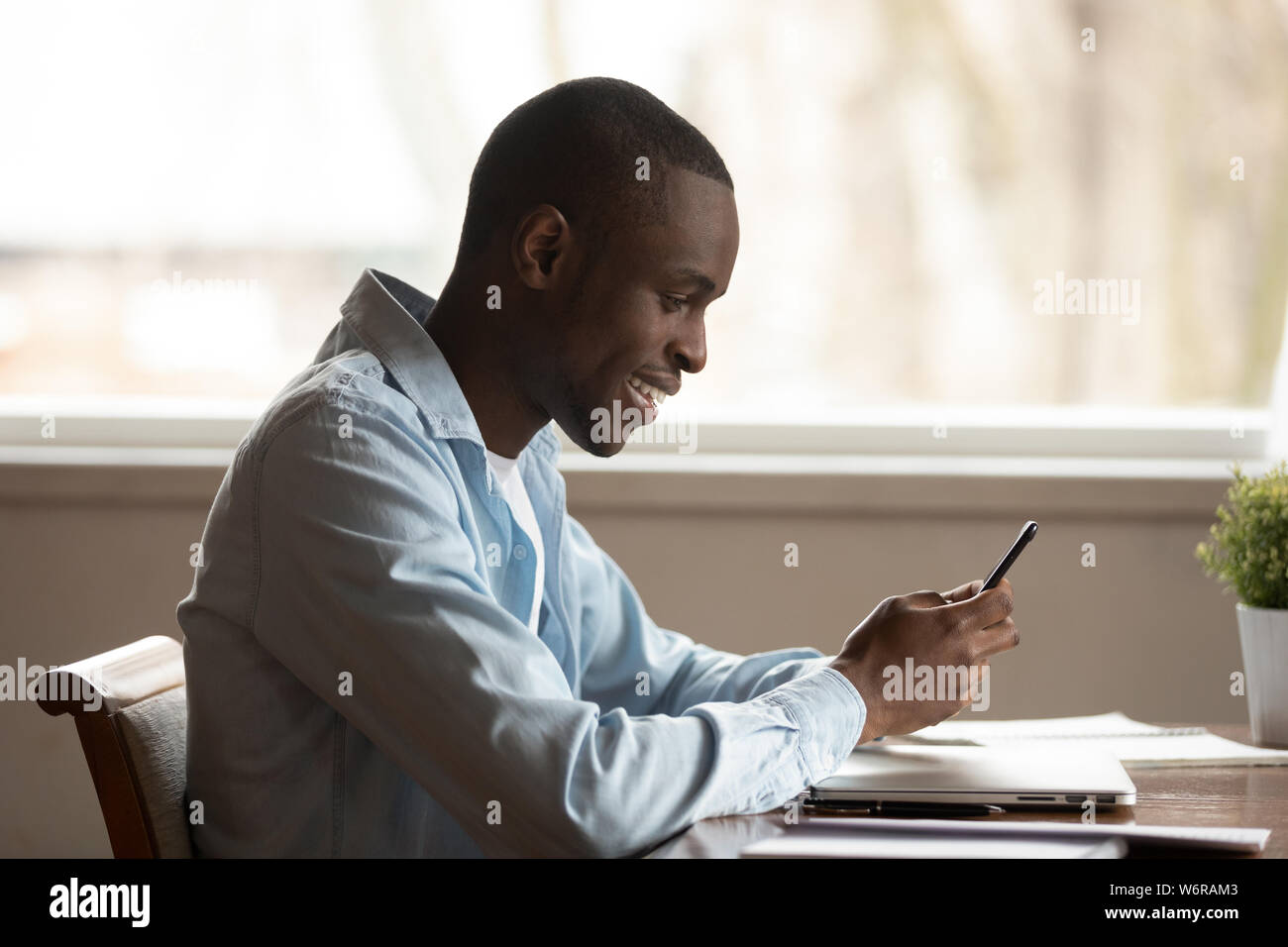 Side view african guy sit at table smiling using smartphone Stock Photo