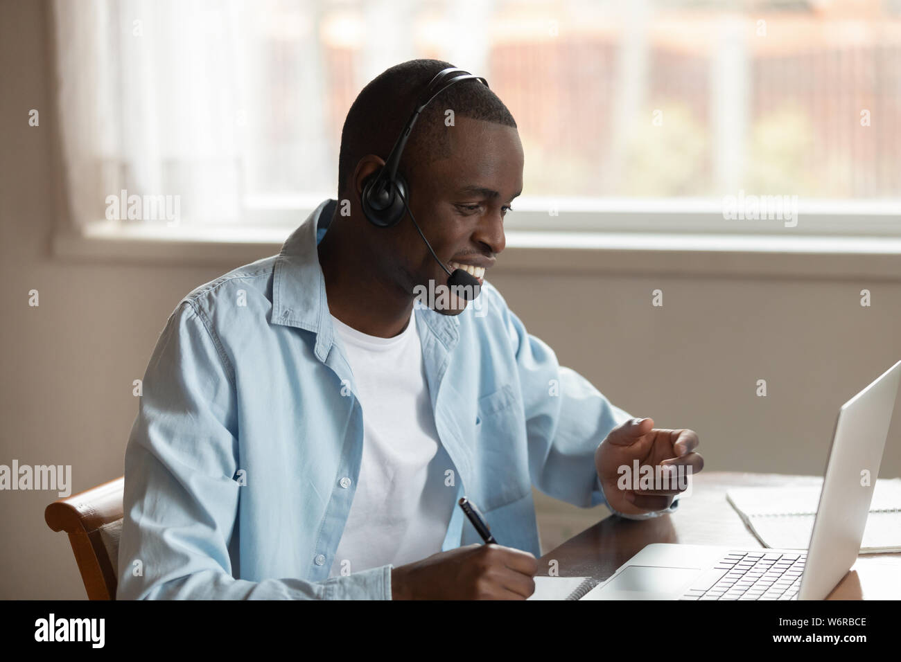African guy wear headset making notes studying online using computer Stock Photo