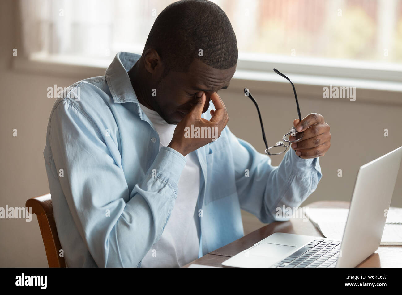 African guy sit near laptop taking off glasses reduce eyestrain Stock Photo