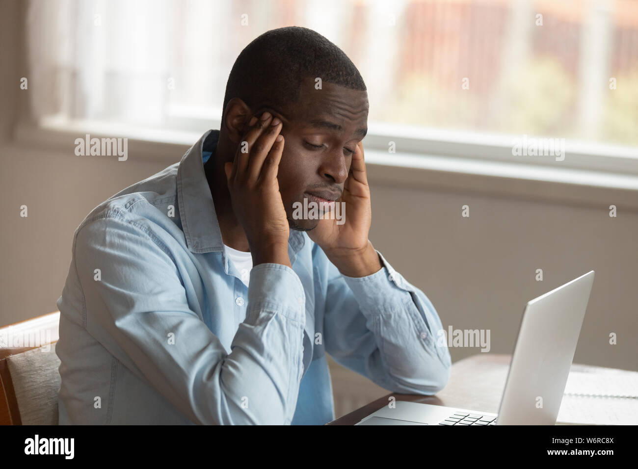 African guy sitting near computer rubbing temples feels unwell Stock Photo