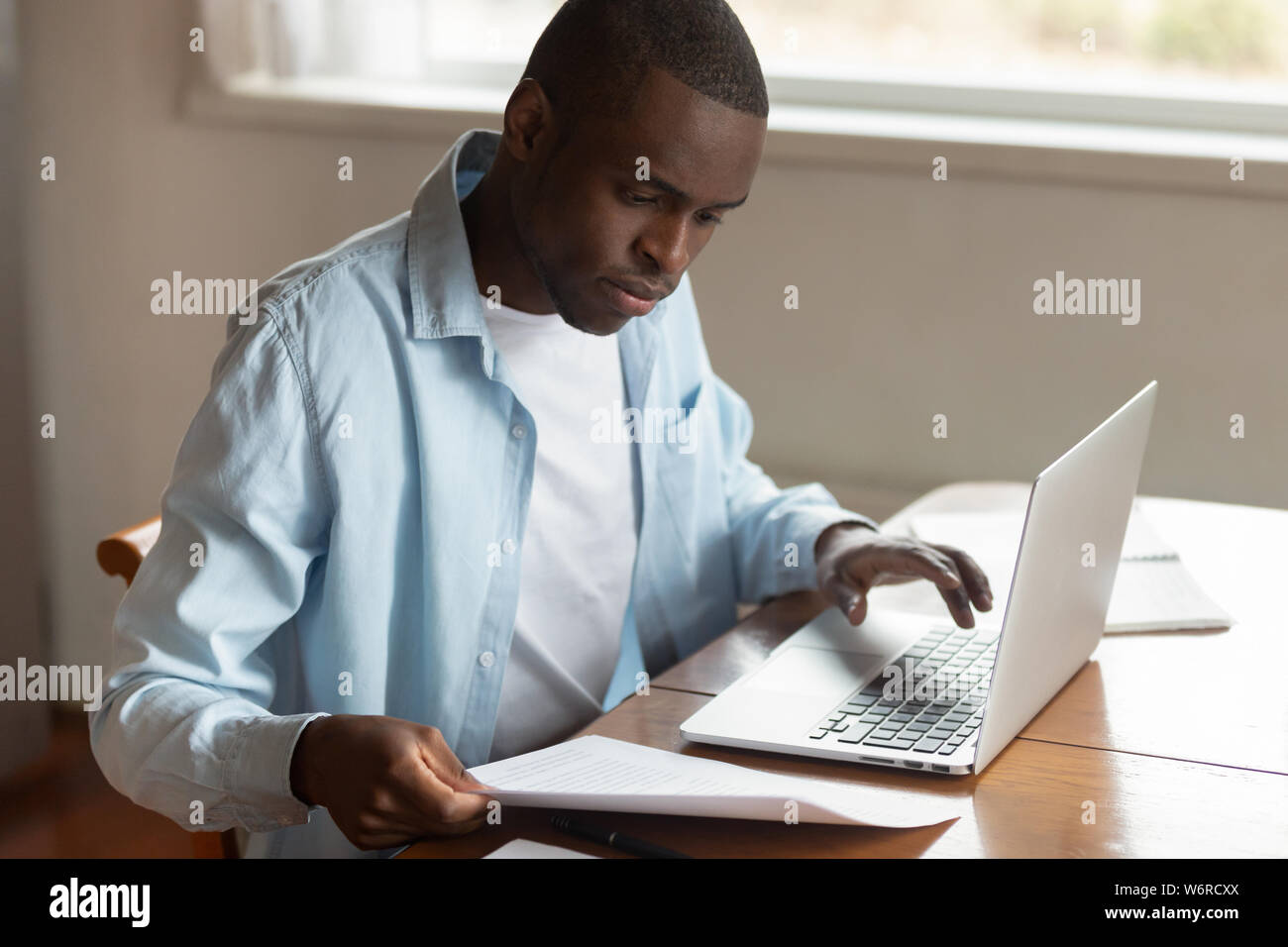African man sitting at table paying household bills using laptop Stock Photo