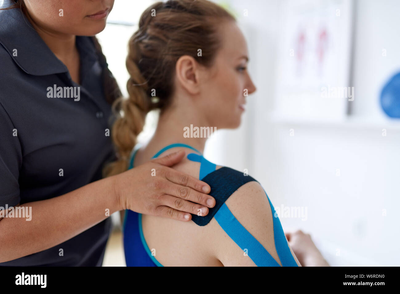 Chinese woman massage therapist applying kinesio tape to the shoulders