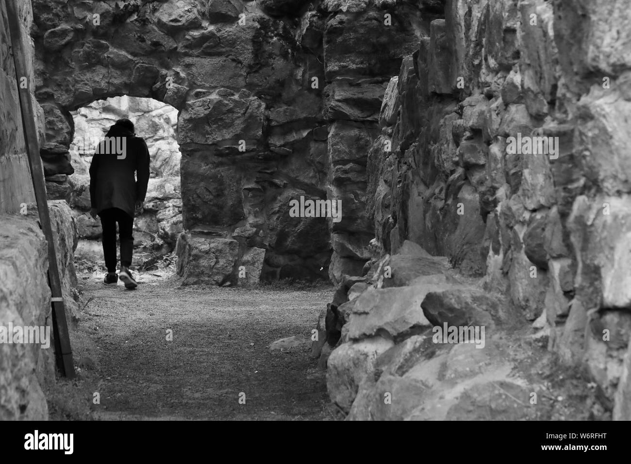 Looking for a way out. A person in old castle at the doorway. Stepping into light. Thick stone walls. Depression, loneliness, lost, anxiety concept. Stock Photo
