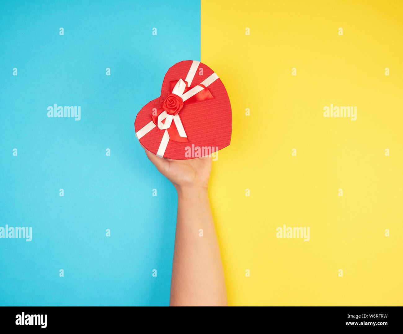 Hand Hold A Paper Closed Red Box In The Shape Of A Heart On A Yellow