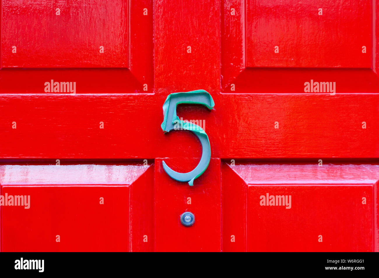 House number 5 in metal covered in plastic on a bright red wooden front door Stock Photo