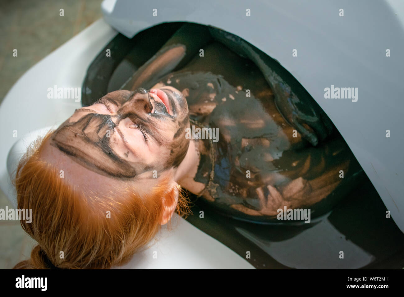 Young woman enjoying mud bath alternative therapy. Woman lies in the ...