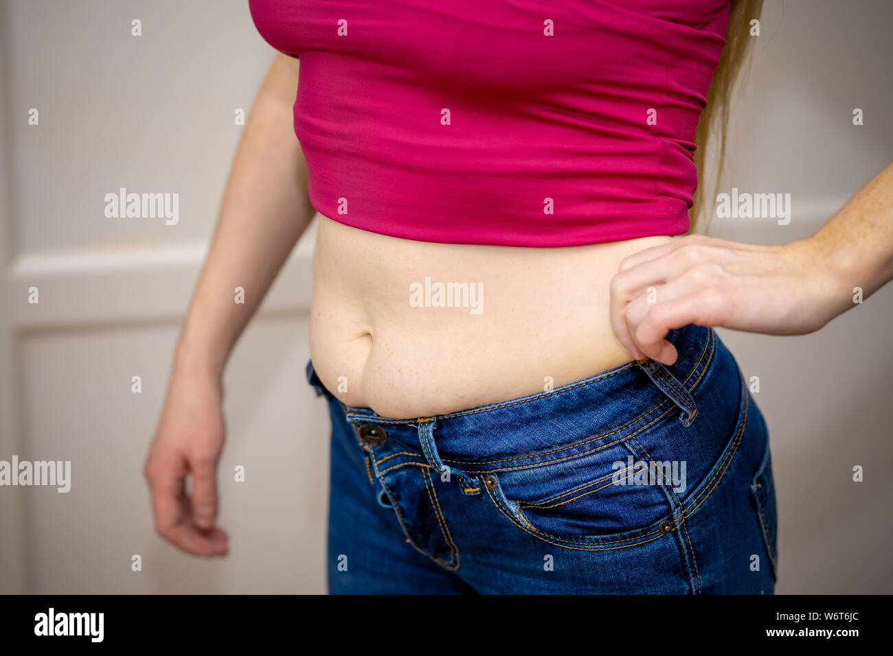 Closeup of woman pinching belly fat. Young slim woman in blue shorts pinching her abdomen. Diet and weight loss concept Stock Photo