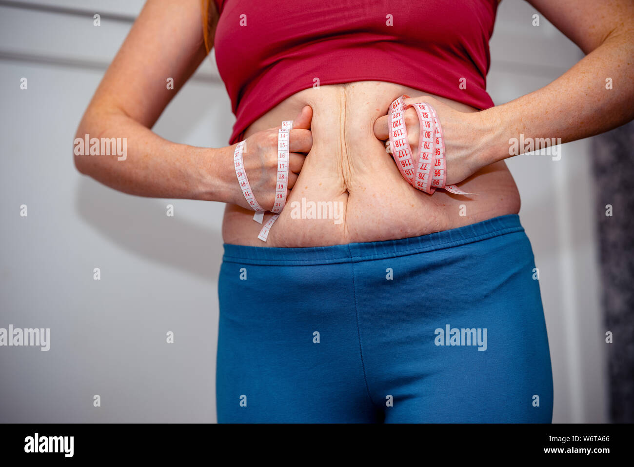 Closeup of woman pinching belly fat. Young slim woman in blue shorts pinching her abdomen. Diet and weight loss concept. Stock Photo