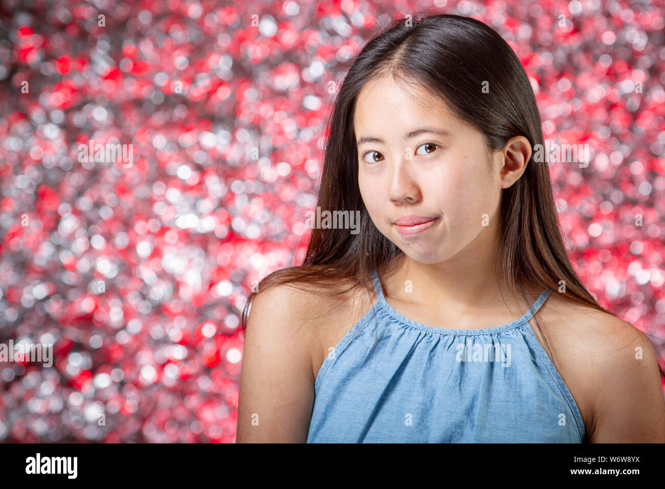 Closeup portrait of beautiful Asian teen girl posing against colorful bokeh background in studio. Stock Photo