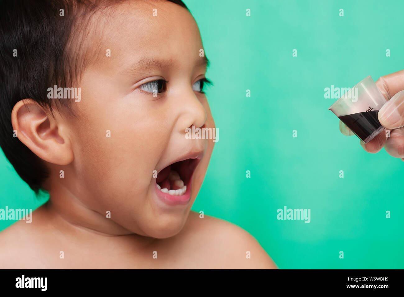 A little kid shocked and yelling at the sight of oral medicine in a cup given by a nurse. Stock Photo