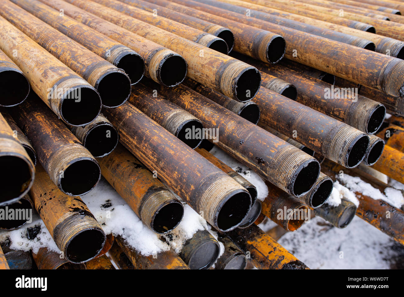 Salvaged pipes and casings are lined up on racks in storage on a ...