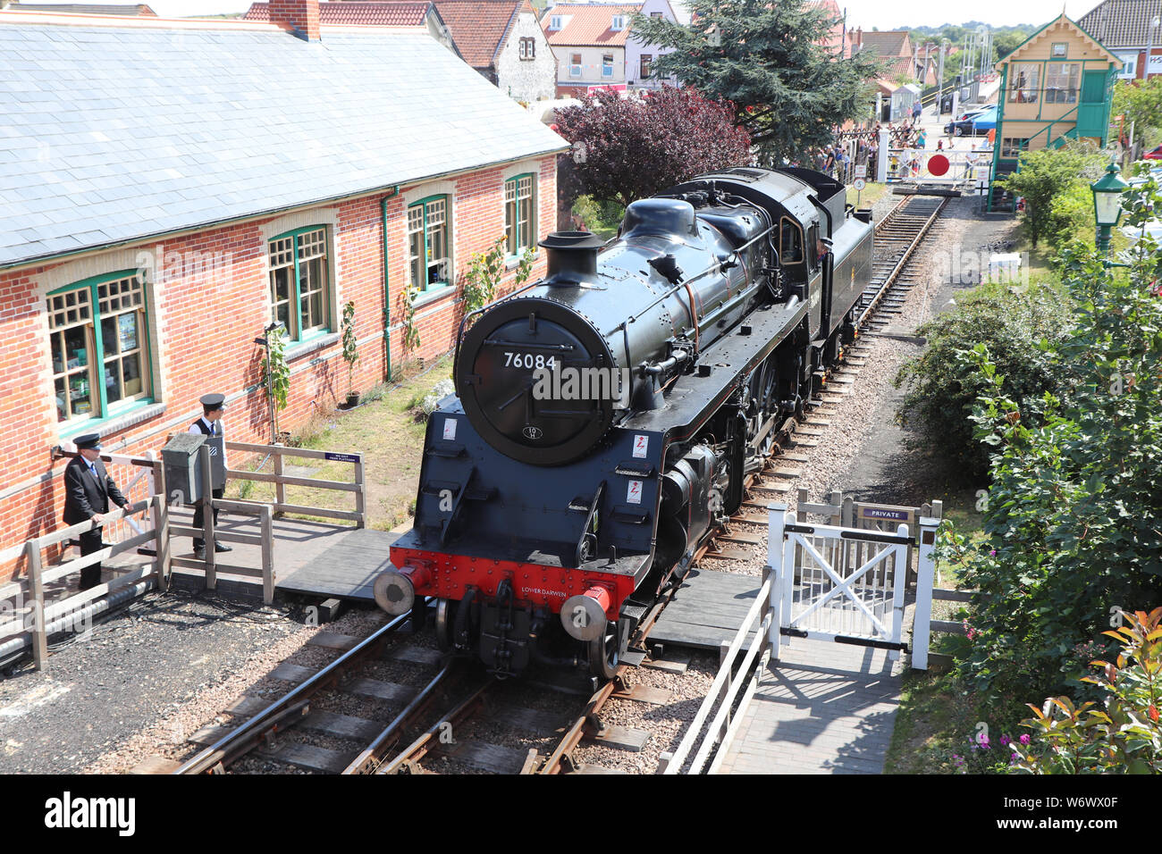Black Steam engine running on the north norfolk railway via the poppy line, passing houses and entering the holt station. Stock Photo