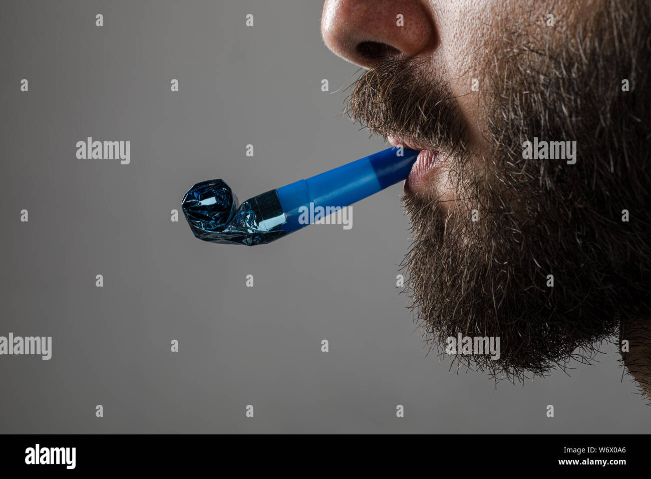 Man with Beard with a Party Horn Blower on Gray Background Stock Photo