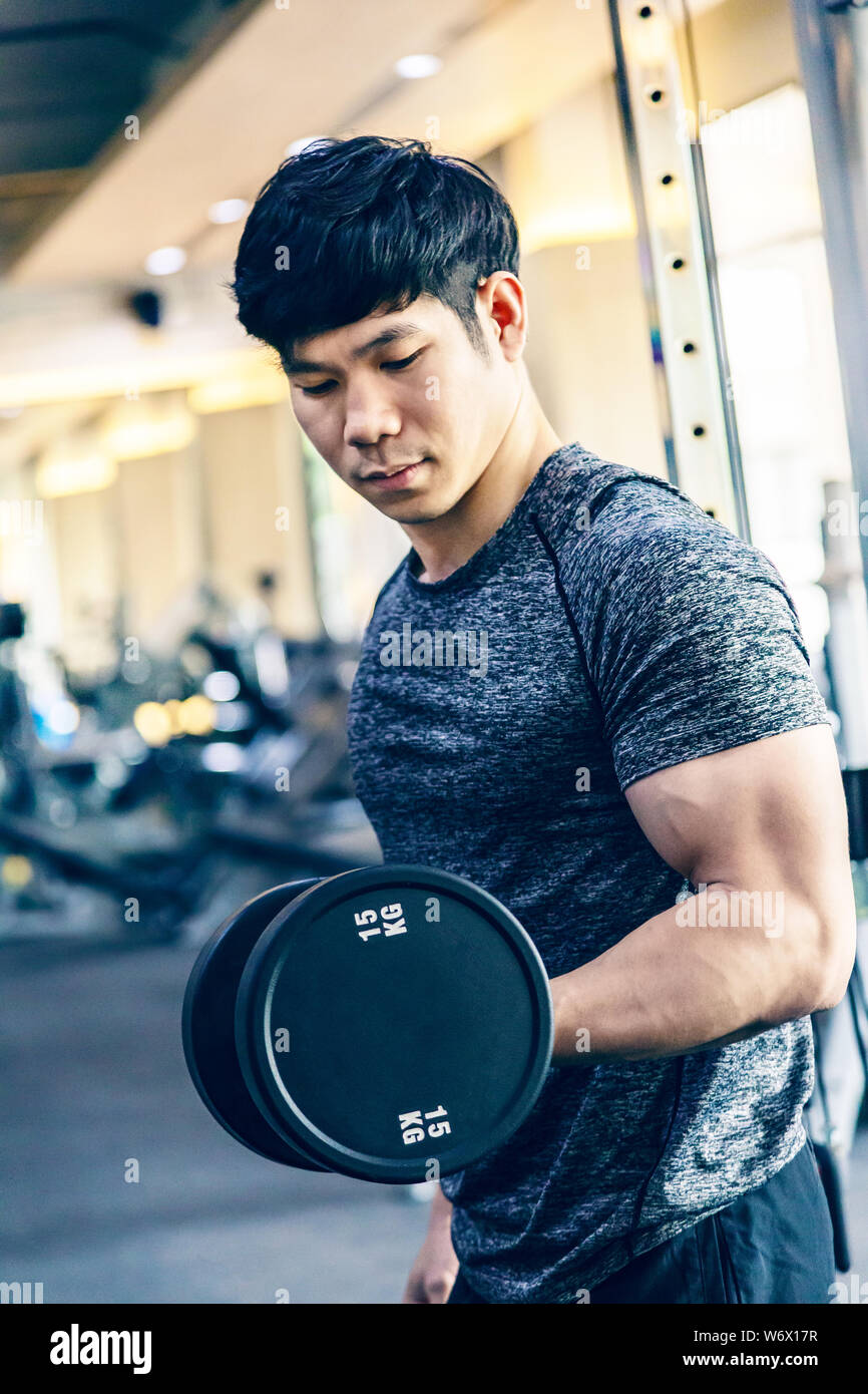 Young Asian man working out lifting heavy dumbbell at a fitness gym, healthy lifestyle Stock Photo