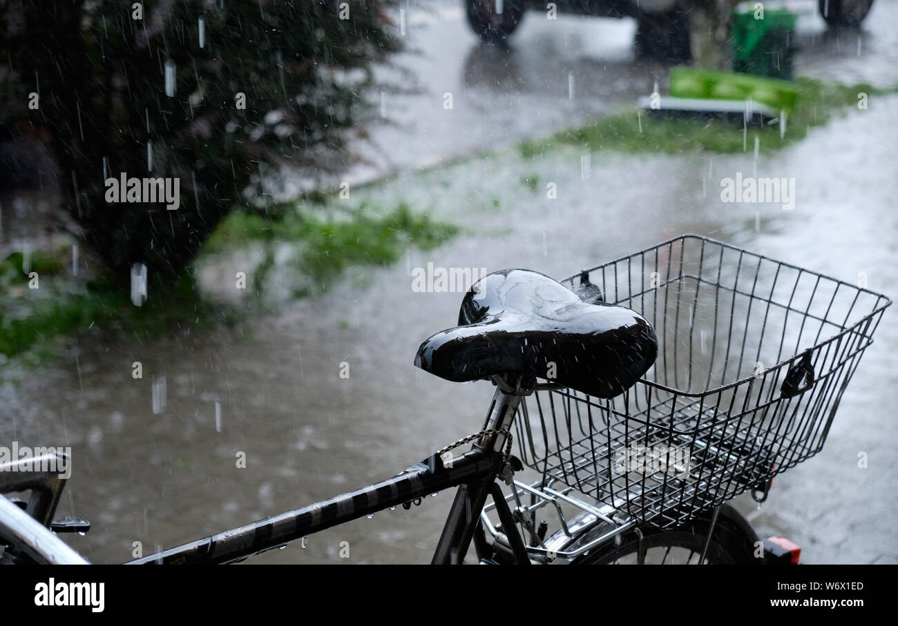 Heavy rain falling on a bicycle seat parked on sidewalk. Focus on the seat and basket, with rest