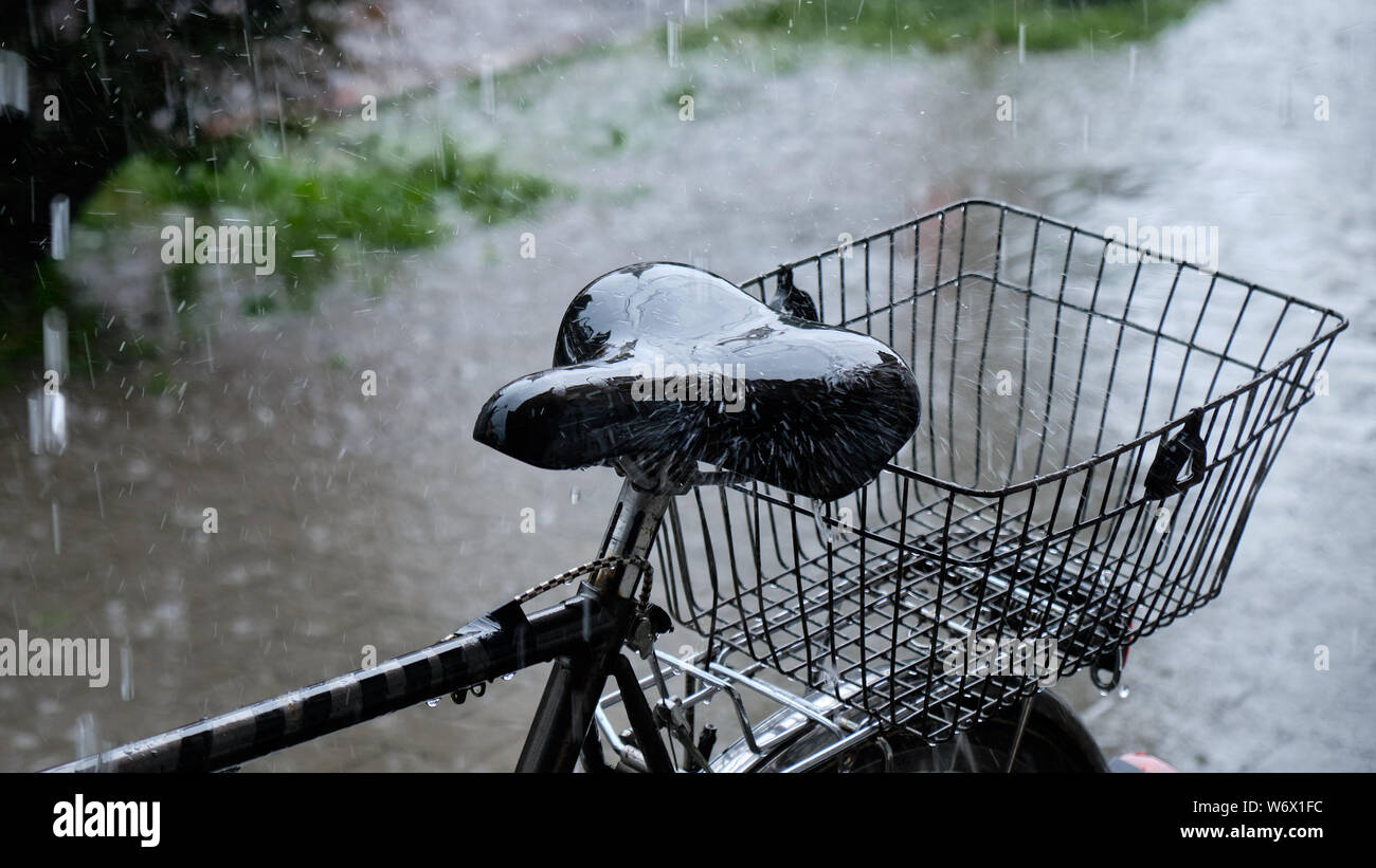 Heavy rain falling on a bicycle seat parked on sidewalk. Focus on the seat, with rest heavily
