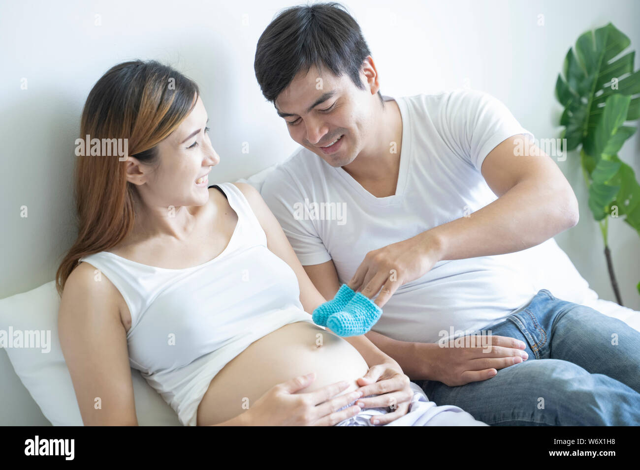 Pregnant couple of husband and wife feels love and relax at home. Young expecting holds baby in pregnant belly. Father take care of pregnant mother. C Stock Photo
