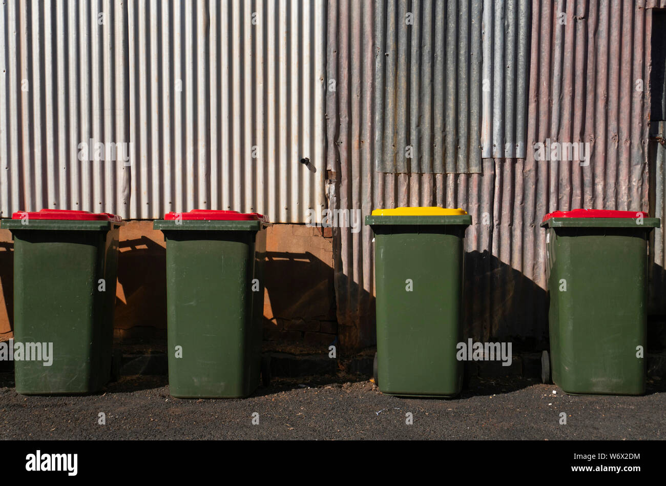 Four rubbish bins waiting to be emptied with corrugated iron wall in