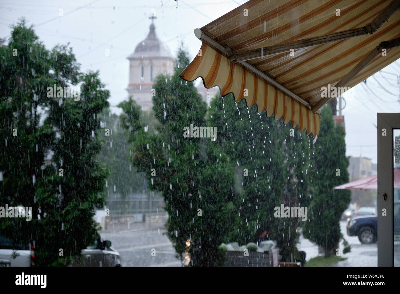 Store front awning dripping during heavy rain storm.  Street view with church in background Stock Photo