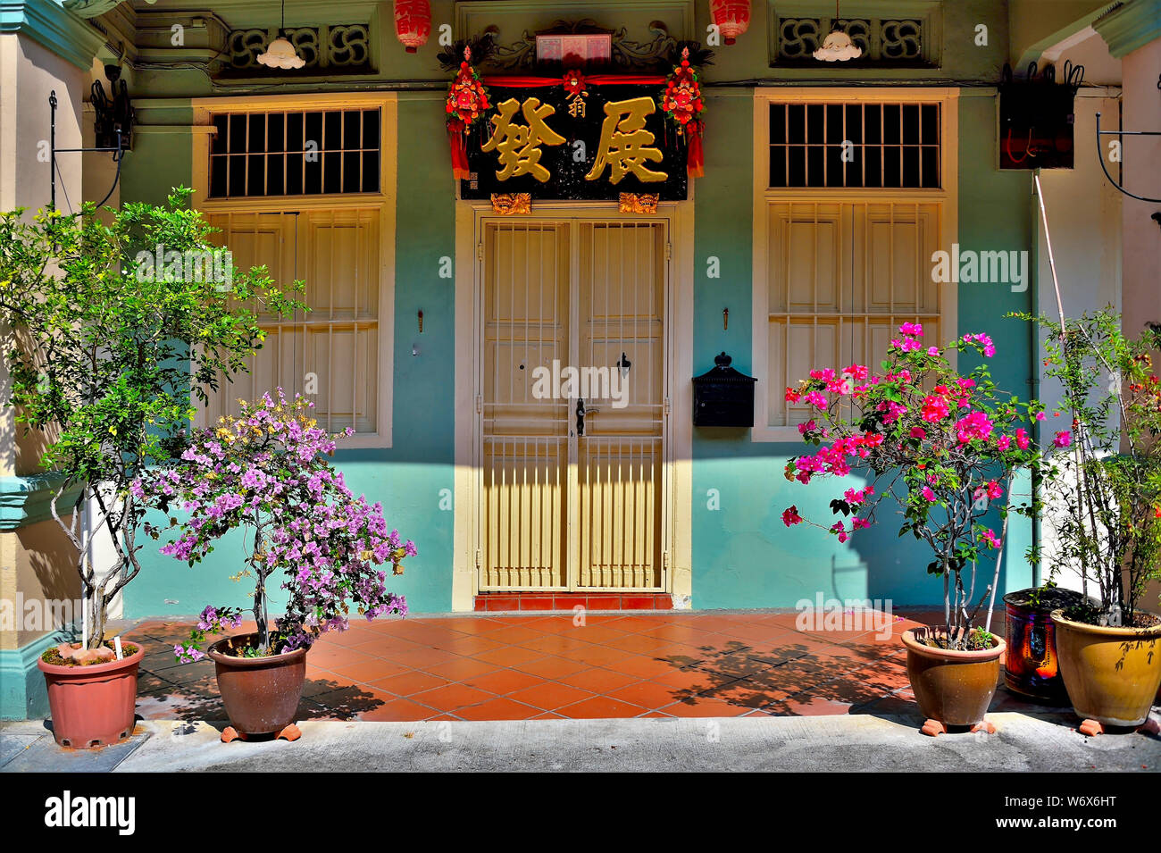 Entrance to traditional Peranakan shop house with cream  door and windows on blue wall with tropical plants in historic Geylang, Singapore Stock Photo