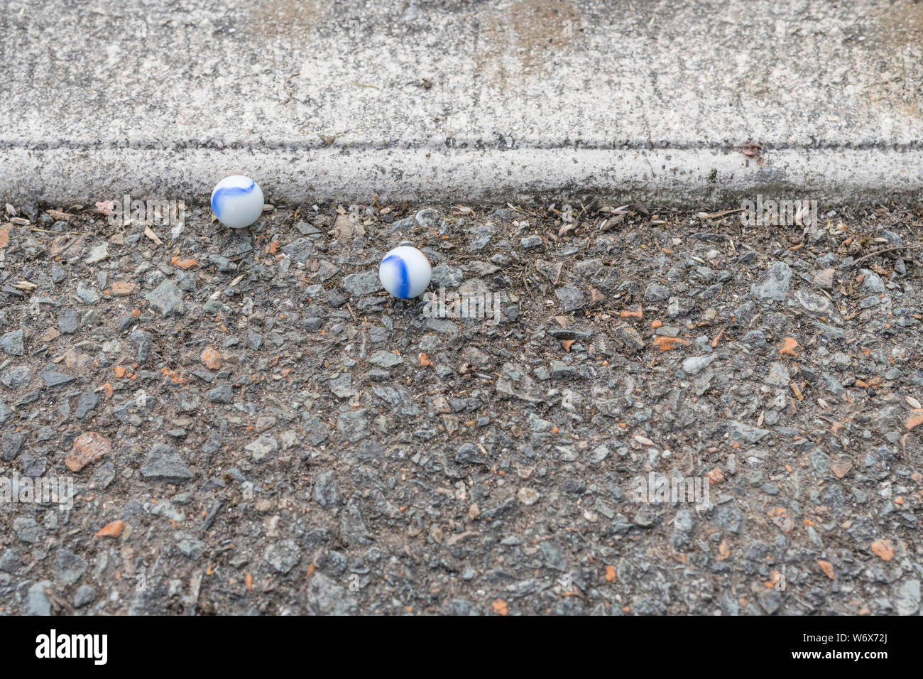 White glass marbles on kerbside tarmac surface. Metaphor something lost, mental health, losing your marbles, childhood games. Stock Photo