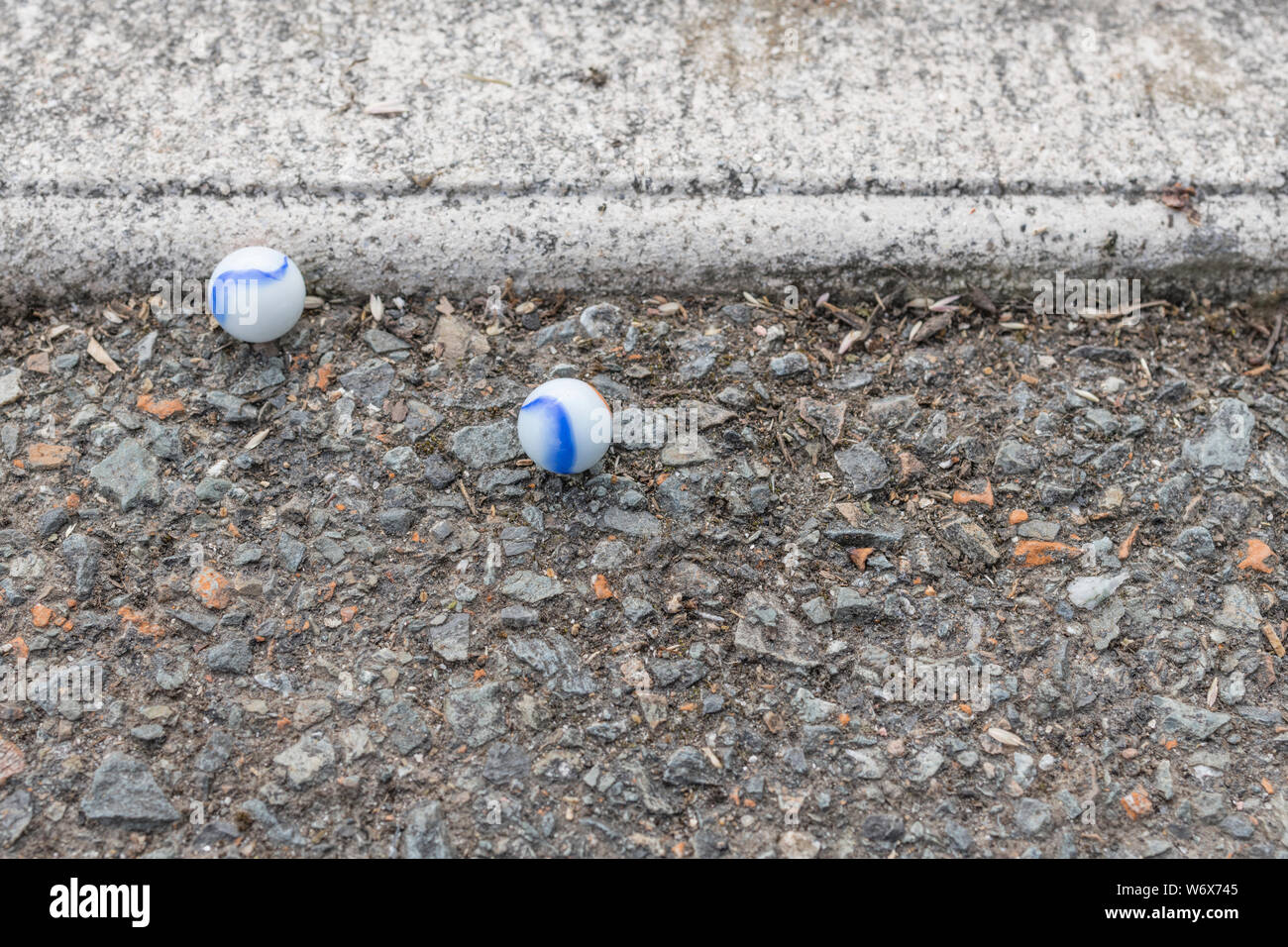 White glass marbles on kerbside tarmac surface. Metaphor something lost, mental health, losing your marbles, childhood games, losing the plot. Stock Photo