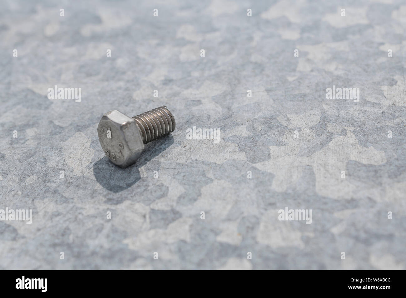Steel hex bolt on zinc coated galvanised sheet metal with spangle evident. Concept metal fixings, industrial fasteners, coated steel, metalwork, bolt. Stock Photo