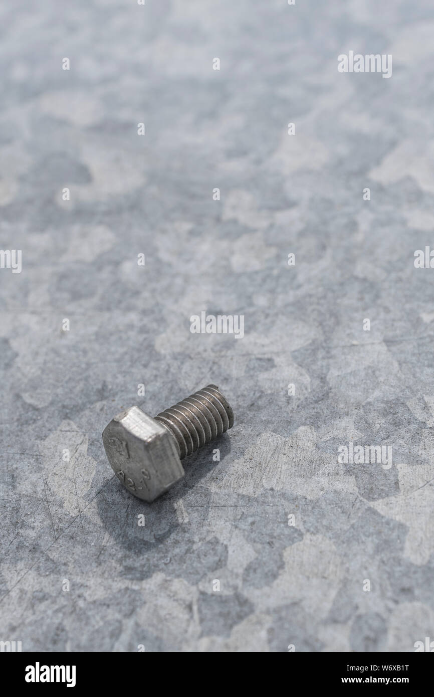 Steel hex bolt on zinc coated galvanised sheet metal with spangle evident. Concept metal fixings, industrial fasteners, coated steel, metalwork, bolt. Stock Photo
