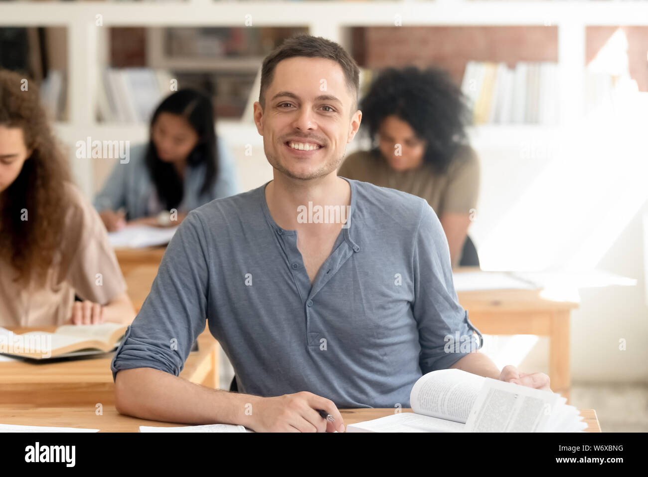 Smiling guy sitting at desk in classroom looking at camera Stock Photo