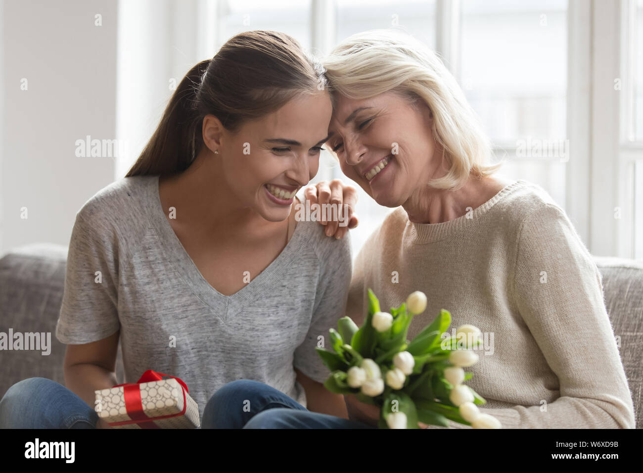 Mother adult daughter sitting on chair with gift and flowers Stock Photo