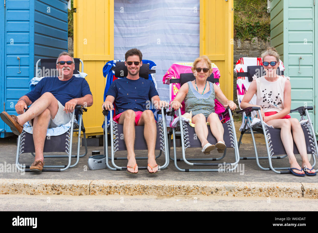Bournemouth, Dorset UK. 3rd Aug 2019. UK weather: overcast and cloudy, but warm and muggy. Beach goers head to the beaches at Bournemouth to enjoy the warm weather. Four people relaxing in sunloungers on promenade outside beach huts.  Credit: Carolyn Jenkins/Alamy Live News Stock Photo