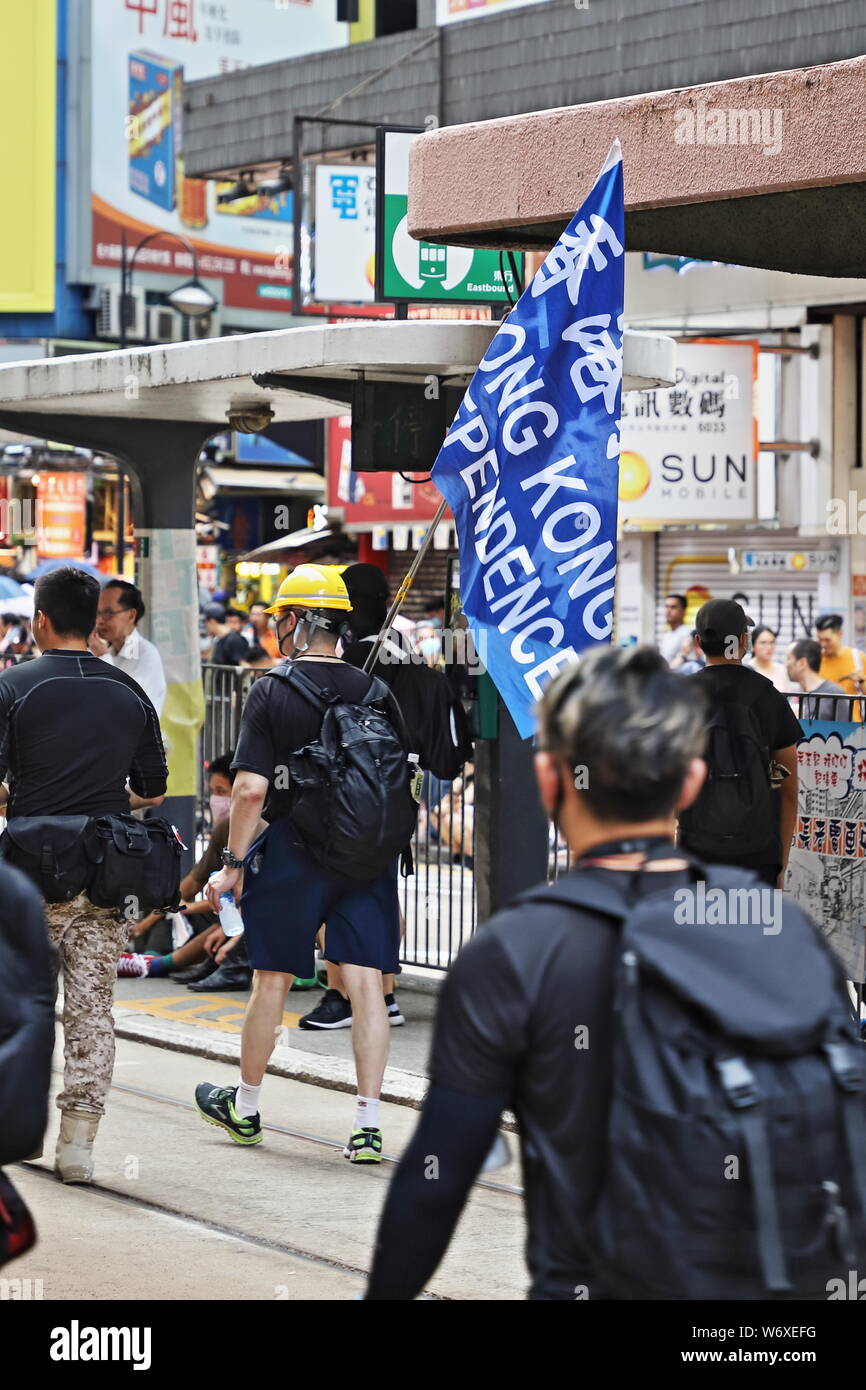 CAUSEWAY BAY, HONG KONG - JULY 25, 2019: Protesters conceal their identity with umbrellas whilst they unbolt and remove pedestrian barriers in advance Stock Photo