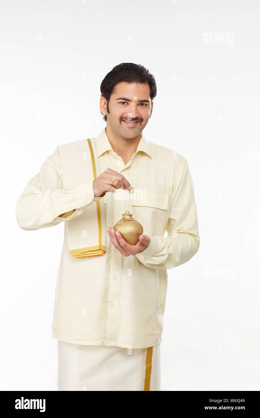 South Indian man inserting a coin into a piggy bank Stock Photo - Alamy
