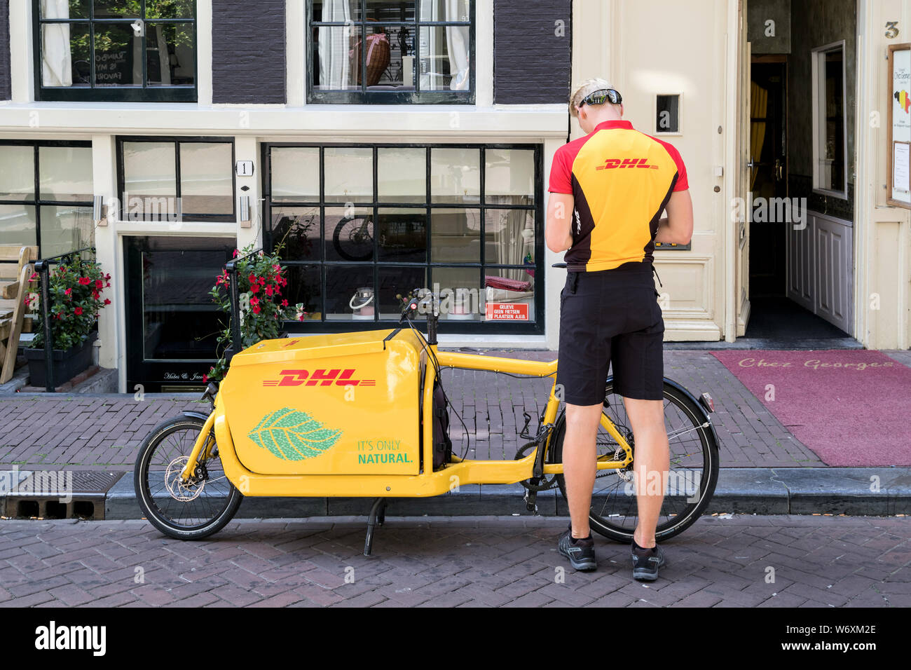 DHL courier with freight bicycle. DHL is a division of the German logistics company Deutsche Post AG providing international express mail services. Stock Photo